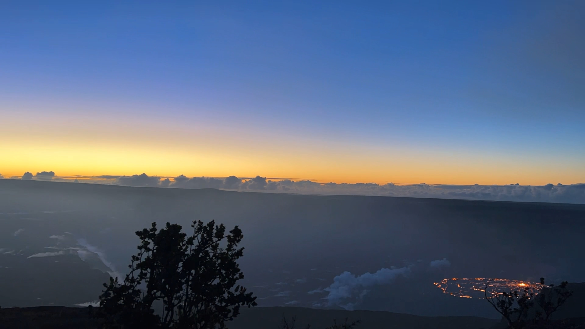 Blue skies and orange sunrise glow bathe the Kilauea caldera right before sunrise